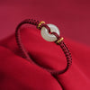 Close-up of a red braided bracelet with a white jade peace buckle on a red background