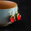A pair of red agate drop earrings with gold-tone settings resting on a ceramic bowl.