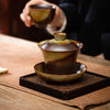 Brown and cream glazed ceramic gaiwan with lid and saucer on a wooden table
