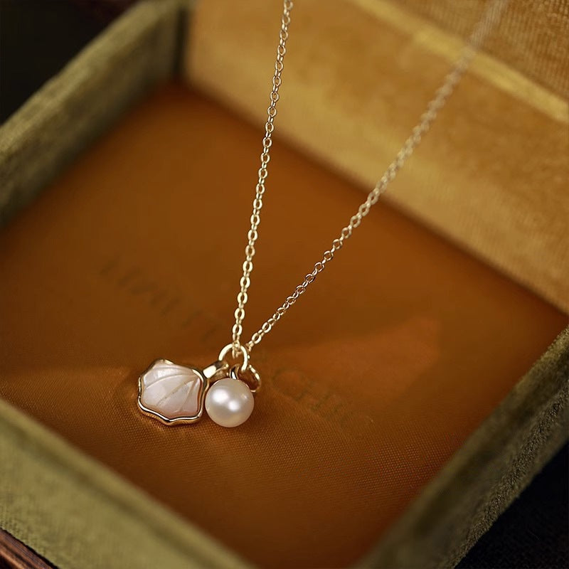 Gold-tone necklace with a white shell pendant and a round pearl resting in a jewelry box