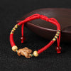 Close up of a red string bracelet with a small carved wooden rat charm