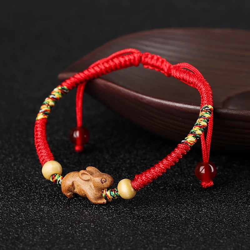 Close up of a red string bracelet with a small carved wooden rat charm