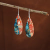 Pair of colorful marbled stone drop earrings hanging from a branch