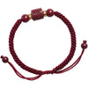 Close up of a red braided bracelet with a square cinnabar bead engraved with Tibetan script