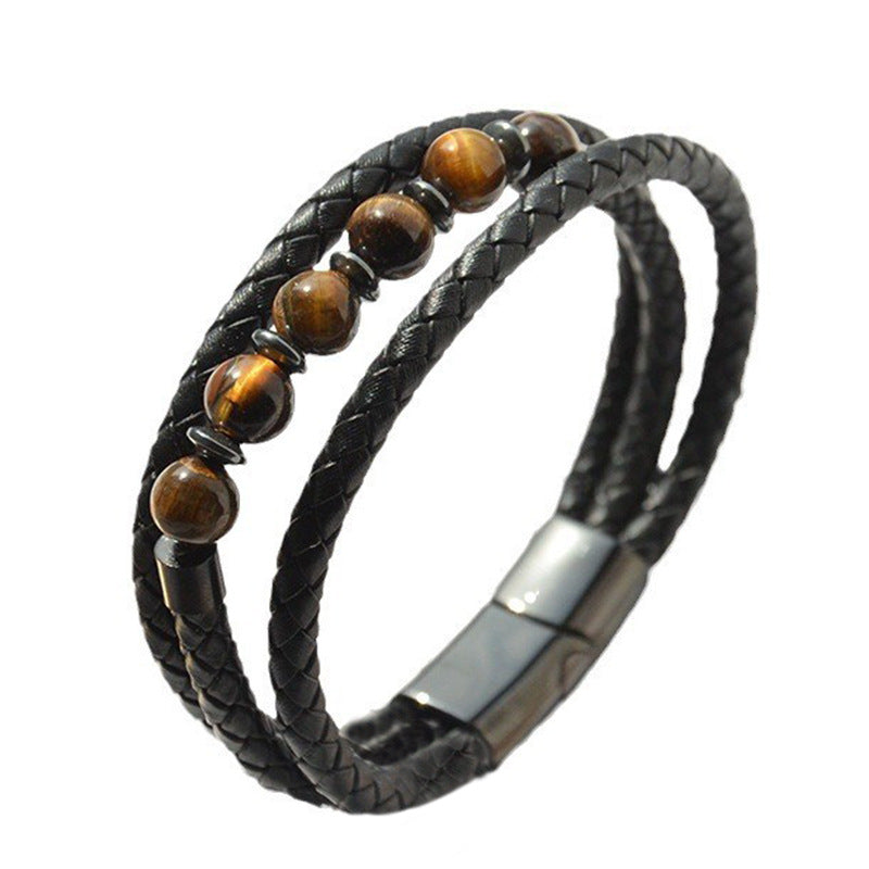 Close up of a black braided leather bracelet with round tiger eye beads resting on a woven surface