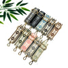 A collection of colorful embroidered nylon shoulder bag straps with gold-tone clips arranged on a white surface.