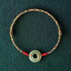 Close up of a multicolored woven rope bracelet with a jade-colored peace buckle charm