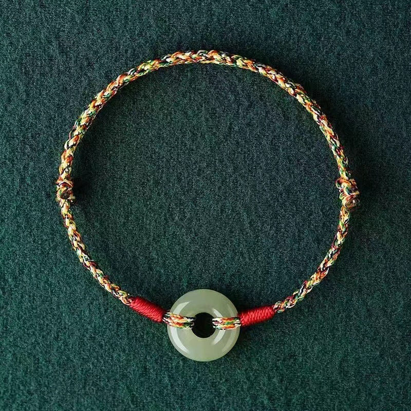 Close up of a multicolored woven rope bracelet with a jade-colored peace buckle charm
