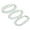 Coiled strand of white and light green Tianshan jade beads on a wooden surface