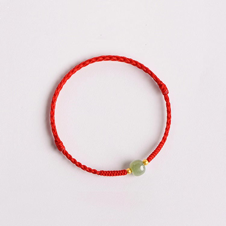 Close up of a red braided cord bracelet with a small light green bead