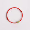 Close up of a red braided bracelet with a small green jade bead on a white background