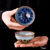 Hand holding a blue and white kiln change ceramic tea cup showing the interior glaze pattern