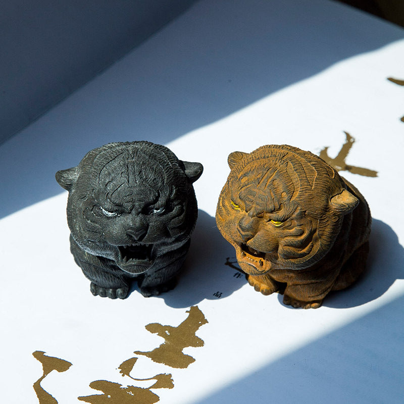 Two small tiger statues sitting on a white surface with gold calligraphy
