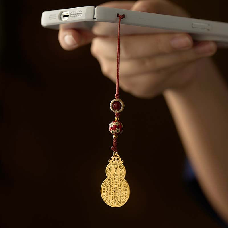 Gold-tone gourd charm hanging from a phone with red cord