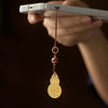 Gold-tone gourd charm hanging from a phone with red cord