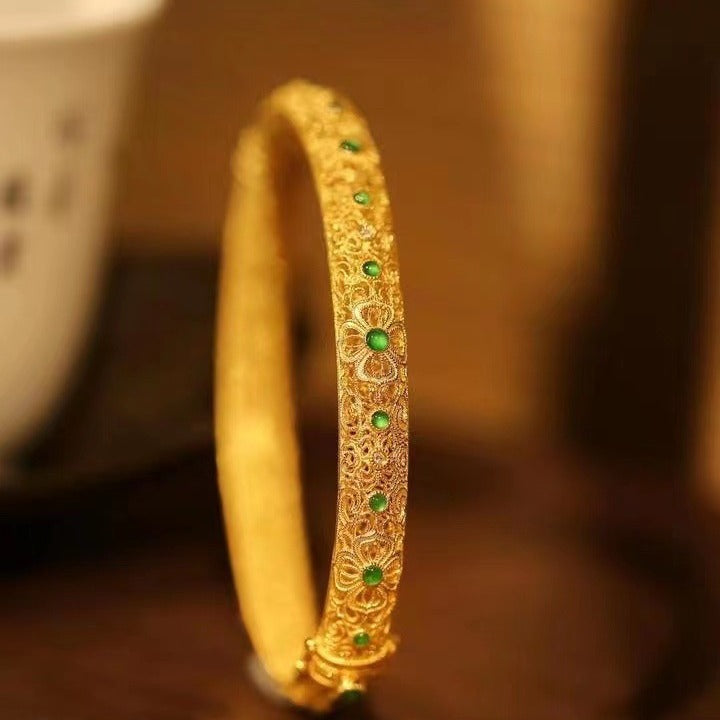 Close up of a gold-tone filigree bangle with small green stones set into the metal