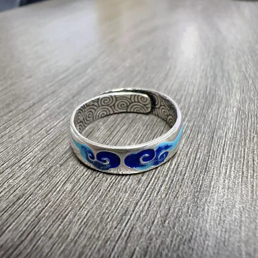 Silver tone copper ring with blue enamel cloud pattern on a wooden surface