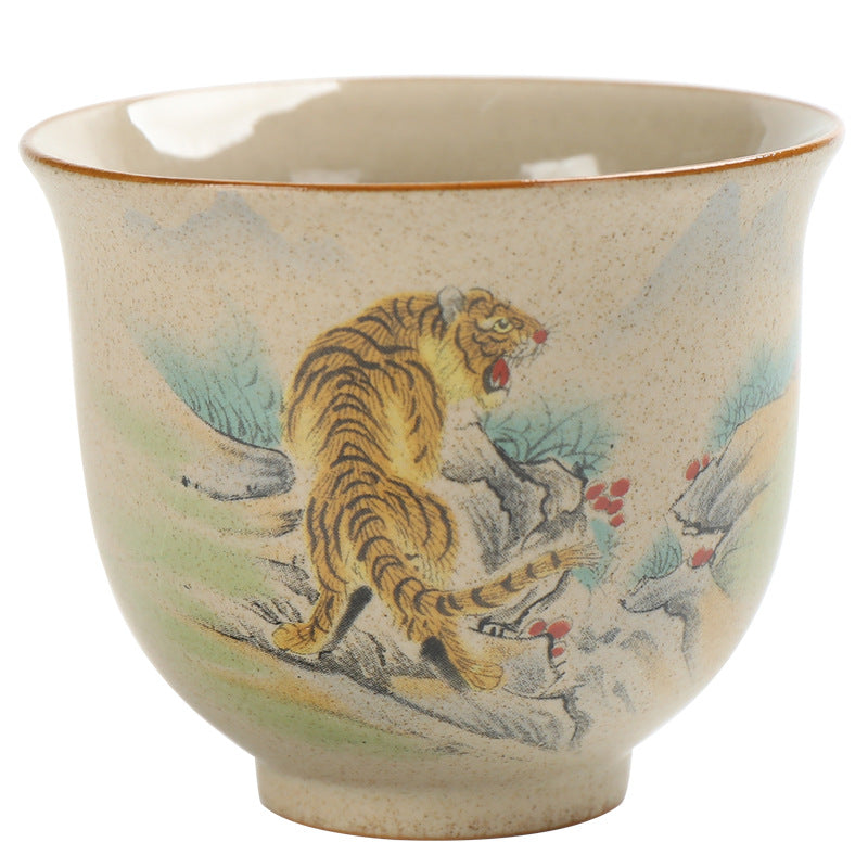 Hand holding a beige ceramic teacup with a painted tiger design