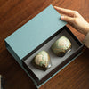 Two green glazed ceramic teacups with lotus pod designs inside a blue gift box