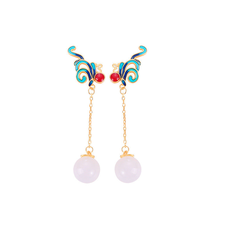 Gold-tone dangle earrings with blue enamel phoenix and white stone drop held in hand