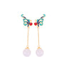 Gold-tone dangle earrings with a blue enamel bird and white stone drop held in hand