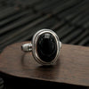 Close up of a silver ring with a black oval stone on a wooden surface