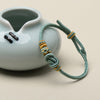Close up of a teal braided cord bracelet with a yuanbao knot