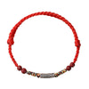 Close-up of a red braided cord bracelet featuring a silver koi fish charm and red cinnabar beads