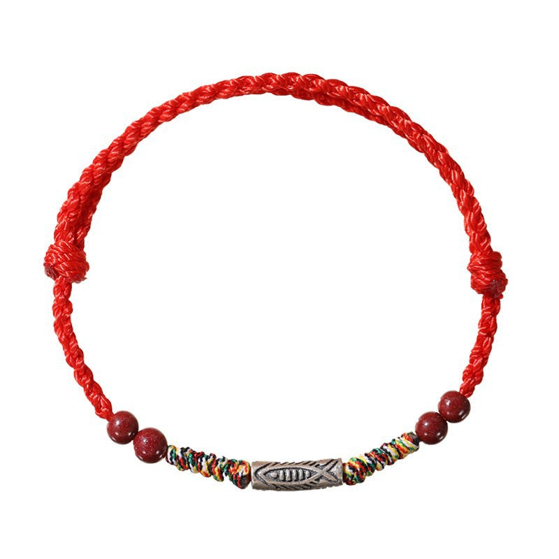Close-up of a red braided cord bracelet featuring a silver koi fish charm and red cinnabar beads