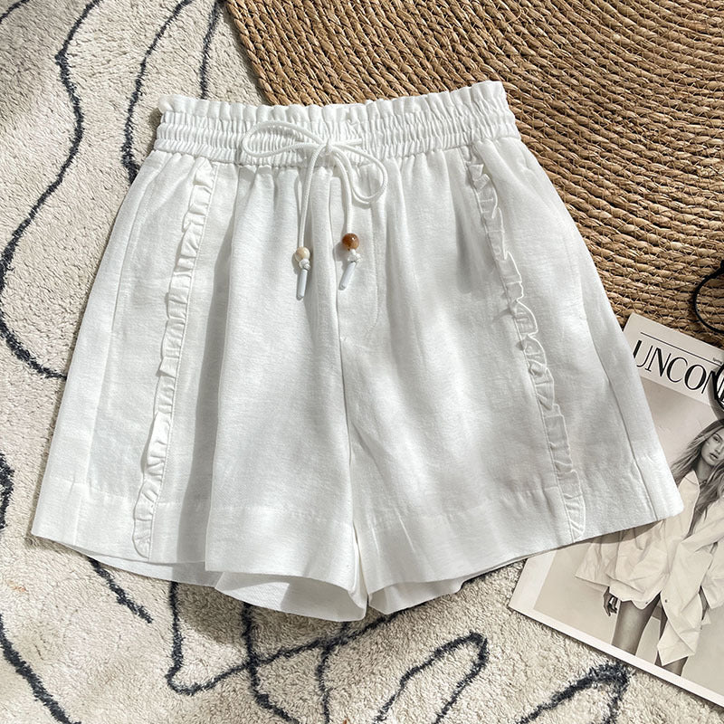 White linen-blend women's shorts with side ruffles and drawstring waist on a textured rug