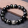 Close up of a black obsidian beaded bracelet with a silver Pixiu charm on a wooden surface