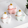Three ceramic cat figurines in pink, white, and green sitting on a book
