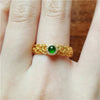 Gold-tone open ring with green stone and scrollwork design on a finger