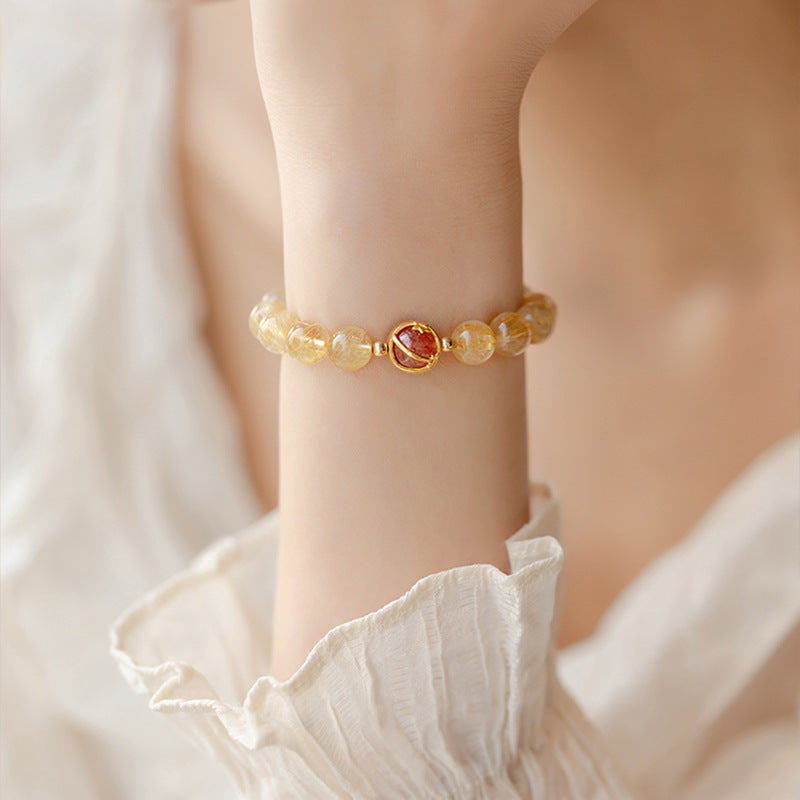 Close-up of a wrist wearing a golden rutilated quartz bracelet with a red center bead