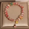Close-up of a pink gradient cat's eye beaded bracelet with a gold butterfly charm on a beige box