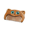 Close up of a small wooden comb carved in the shape of a cat face with blue eyes