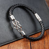 Black braided leather bracelet with a silver infinity knot clasp on a wooden surface