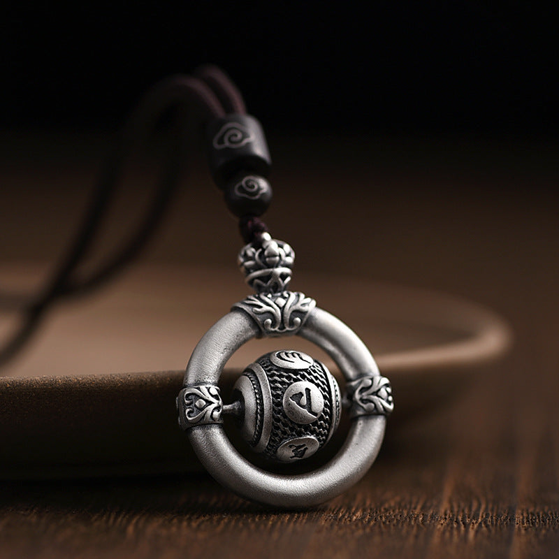 Close-up of a silver-tone copper pendant with a rotating center bead on a brown cord