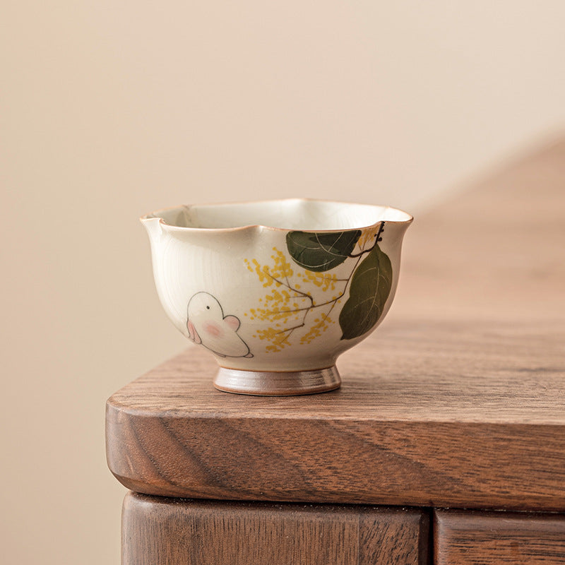 Small hand painted ceramic teacup with rabbit and flower design on wooden table