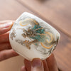 White ceramic teacup with gold and green dragon relief held in hand