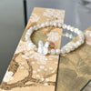 Close up of a white pearl bracelet with a mother of pearl rabbit charm on a wooden surface