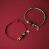 Two braided bracelets with jade beads and a lotus charm on a red background