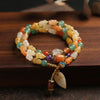 Three-wrap Golden Silk Jade bracelet with colorful beads and a hanging gourd charm on a wooden surface