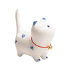 White ceramic cat figurine with blue spots and a red collar standing on a wooden surface