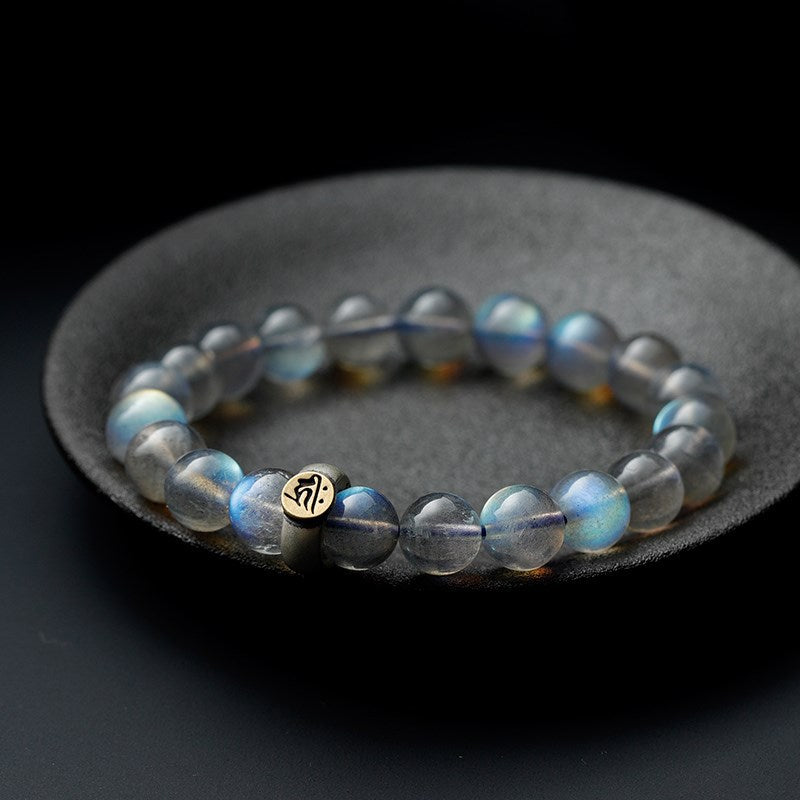 A moonstone bead bracelet with a gold charm resting on a dark stone dish