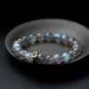 A moonstone bead bracelet with a gold charm resting on a dark stone dish