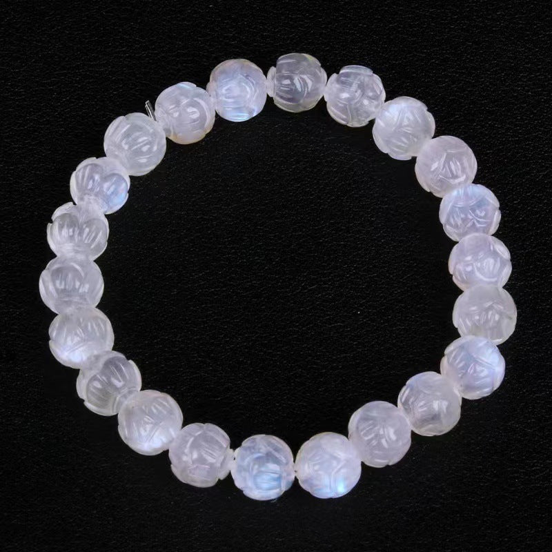 Close-up of a white moonstone bracelet with carved lotus flower beads on a black background