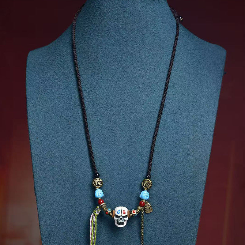Close-up of a black woven cord necklace with a white skull pendant and blue beads on a mannequin bust