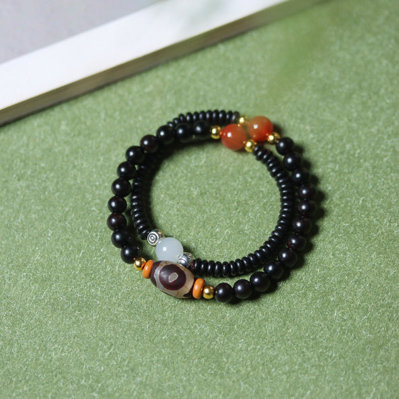 Double wrap wood bracelet with black beads and a brown patterned Dzi bead on a green background