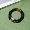 Double wrap wood bracelet with black beads and a brown patterned Dzi bead on a green background